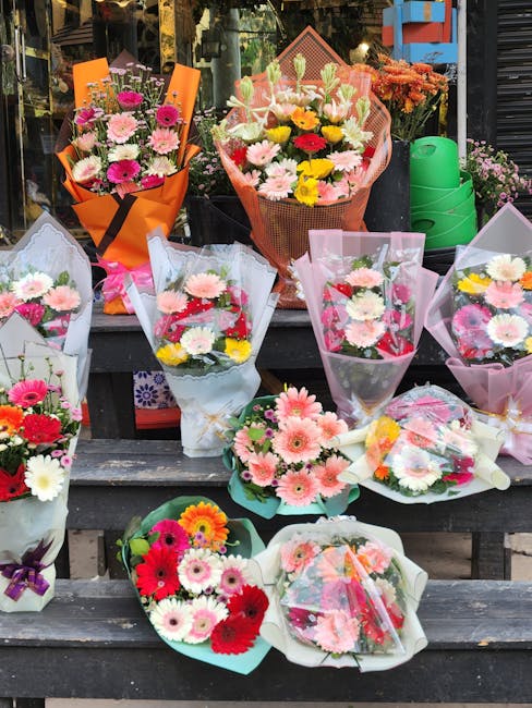 A display of various floral bouquets arranged on a wooden outdoor surface, featuring a mix of colorful flowers such as pink, white, red, and yellow daisies, carnations, and gerbera daisies. The bouque