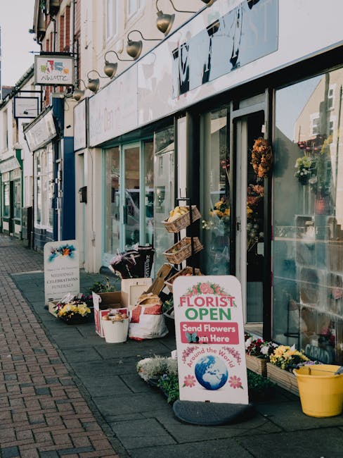 A floral display outside Cheam Florist, featuring a variety of fresh flowers arranged in white buckets and wooden crates on the sidewalk. The flowers include brightly coloured roses, chrysanthemums, a