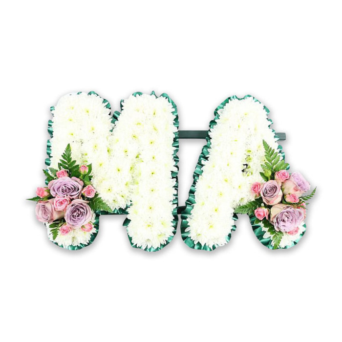 A personalised funeral letter tribute in the shape of the word MA is presented against a bright white background, giving the design a serene, almost luminous quality. Each of the two capital letters is expertly covered in hundreds of fresh white chrysanthemums, their small, rounded petals overlapping to form a soft, cushiony texture that feels comforting just to look at. The blooms sit close together with no gaps, creating an unbroken field of white that symbolises purity, remembrance, and the gentlest kind of farewell. Around the edges, a deep green satin ribbon has been carefully folded into fine pleats and ruffles, hugging every angle and curve of the M and the A. This rich emerald border frames the letters beautifully, adding definition and a sense of craftsmanship that a Cheam florist would take real pride in. At the base of the left upright of the M and the right upright of the A, two coordinated floral sprays provide a touch of romance and colour. Soft blush-pink roses and muted lilac roses are gathered with dainty pink spray roses, some blooms open and others in bud, so the eye reads a natural rhythm of shapes and tones. A single airy fern frond in each cluster extends outward, adding lightness and a natural, garden-like feel, as though the tribute had been freshly gathered from a peaceful green space near Nonsuch Park. The arrangement's overall mood is tender and reflective, evoking gratitude, memories, and the intimate bond between a mother and her family, expressed thoughtfully through traditional white funeral flowers with pastel accents.