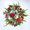 From a top-down view against a pure white background, this hand-tied bouquet looks like a rich, circular tapestry of red, white, and green, as if freshly arranged on the workbench of a Cheam florist. At its centre, velvety crimson roses draw the eye, some still in tight bud promising to open, others partway unfurled so their layered petals curl softly outward. Clustered around them are ruffled carnations in vivid fuchsia and ruby-red tones, their frilly edges creating a plush, almost cloud-like texture that feels festive and generous. Threaded between the bold reds are dainty white spray chrysanthemums or similar daisy-like flowers, each with a bright eye and crisp petals that lift the palette and add a cheerful brightness. Tiny stars of white gypsophila-baby's breath-float through the gaps, forming a misty veil that softens every transition and makes the bouquet feel light and airy despite its fullness. Surrounding and cradling the blooms is a lush mix of foliage: broad, pointed dark-green leaves from lilies or alstroemeria give structure, while rounded, silvery eucalyptus leaves weave in and out with a cool blue-green sheen, adding a modern, slightly wild garden feel that would not be out of place near Cheam Park. The flowers appear fresh and dewy, as though just conditioned for same-day delivery across Cheam and the surrounding streets. The composition is balanced yet exuberant, radiating affection and joy, ideal for sharing love on an anniversary, surprising someone on their birthday, or sending a heartfelt get well wish that feels like a warm embrace in floral form.
